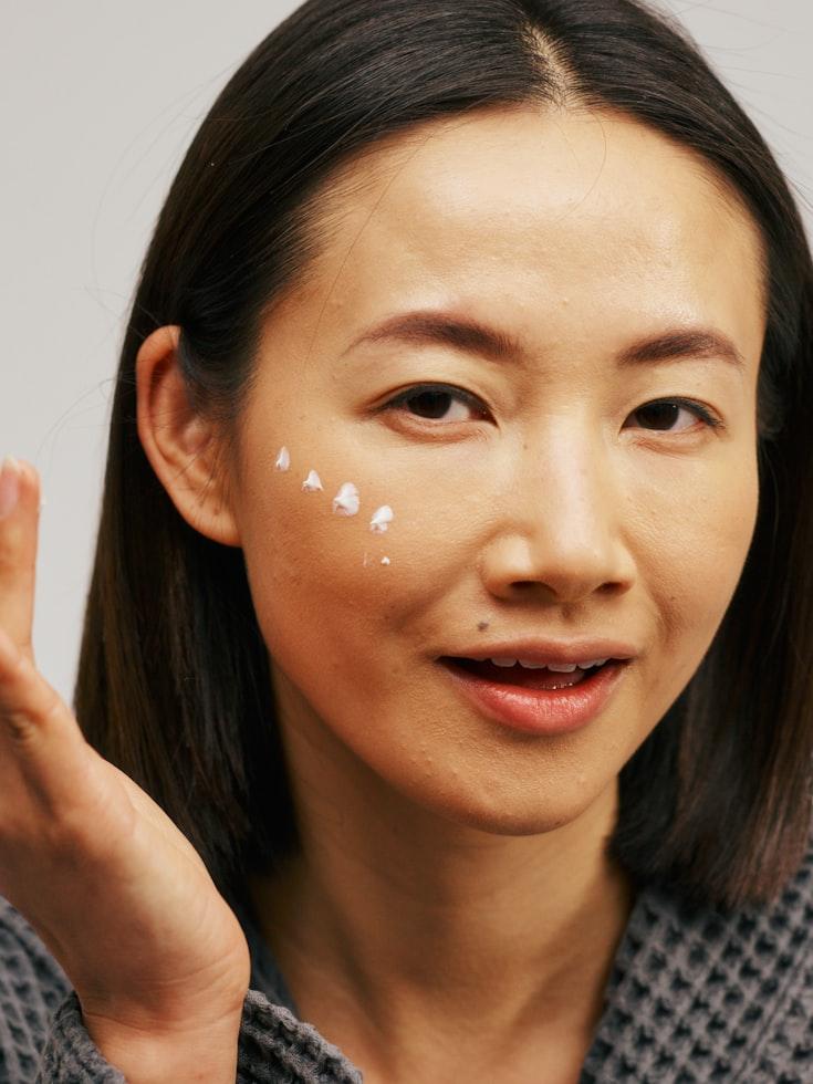 Woman applying cream to her face with a neutral background